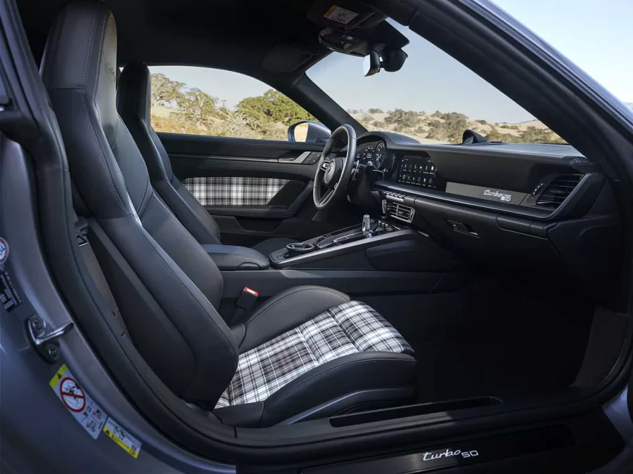 O interior do 911 Turbo 50 Years apresenta detalhes históricos como o tartan McKenzie nos assentos e portas, além de cintos de segurança e costuras decorativas em Turbonite, reforçando o design exclusivo.