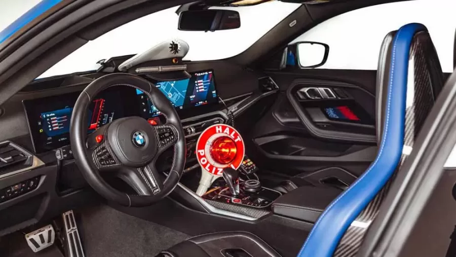 O interior do M2 modificado inclui um pedal de alumínio, paddle shifters maiores e um sinal de "Halt Polizei", complementando a proposta de visual de viatura e funcionalidade esportiva.