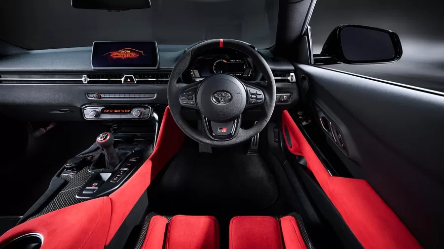 Interior do Supra Final Edition tem bancos Recaro, detalhes em Alcantara e cintos vermelhos, destacando a esportividade enquanto mantém conforto e foco na condução.