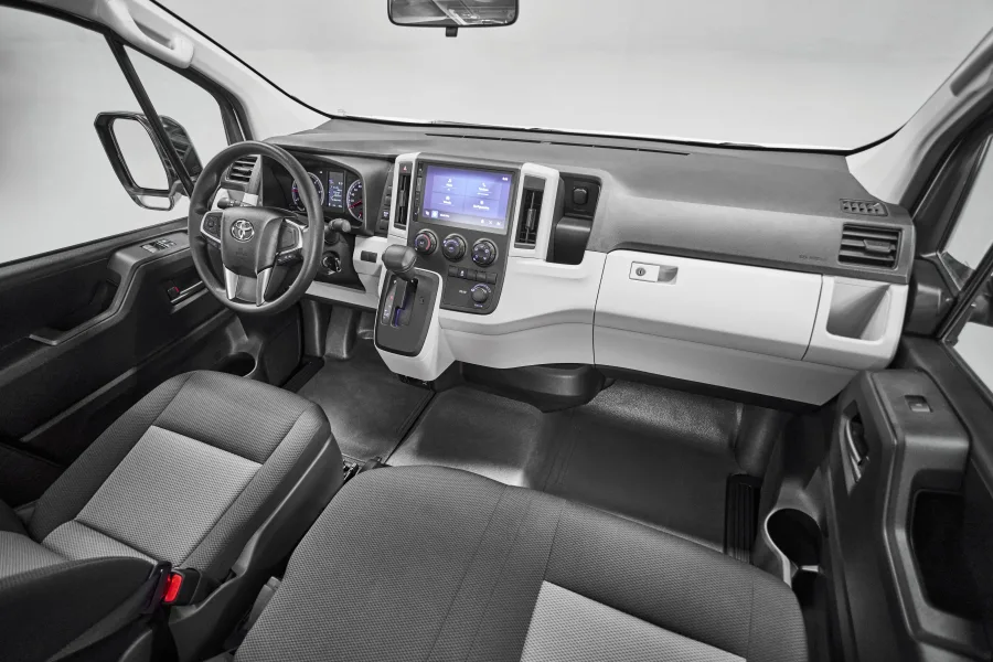 A Toyota Hiace tem interior funcional, espaço para 15 passageiros, bancos simples e ar-condicionado com saídas distribuídas, garantindo conforto térmico, mas sem luxo.